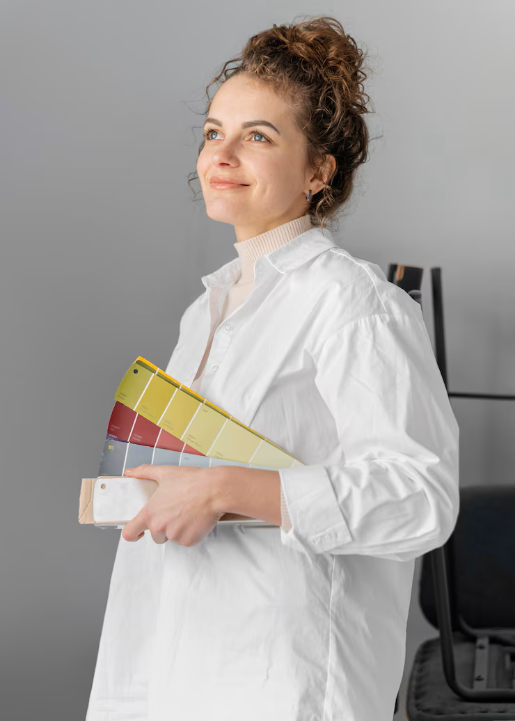 Mulher sorridente escrevendo em um caderno, sentada em um sofá cinza em uma sala iluminada.