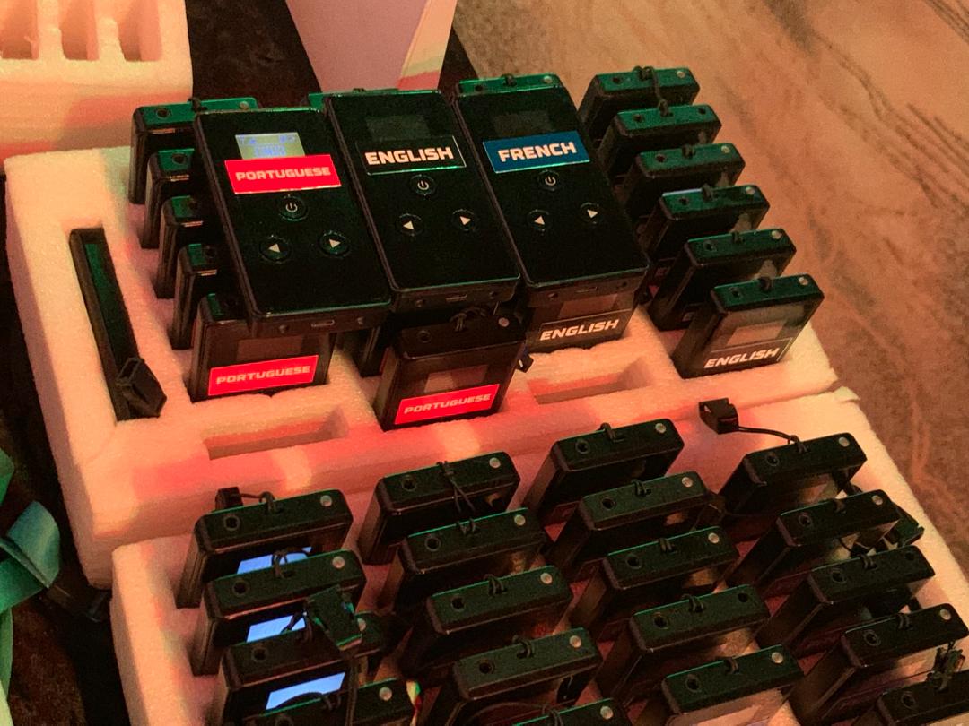 Smiling professional woman in glasses working at a computer in a busy office environment.
