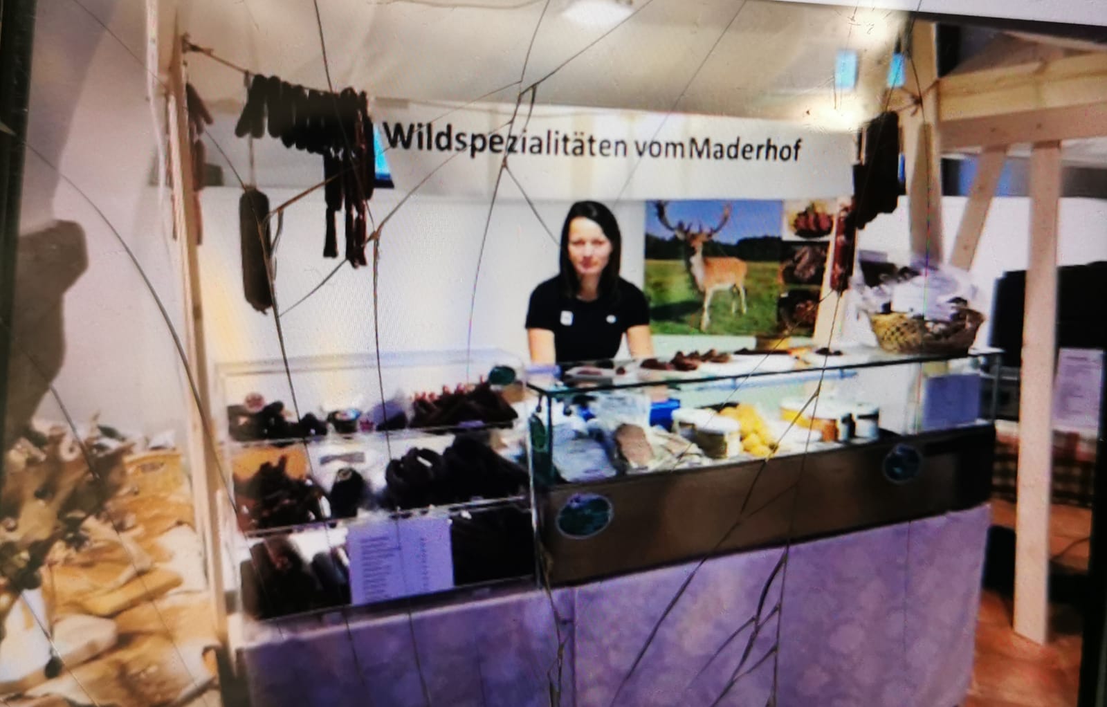 Verkaufsstand mit Wildspezialitäten, beschriftet mit 'Wildspezialitäten vom Maderhof', eine Frau steht hinter der Vitrine mit Wurstwaren.