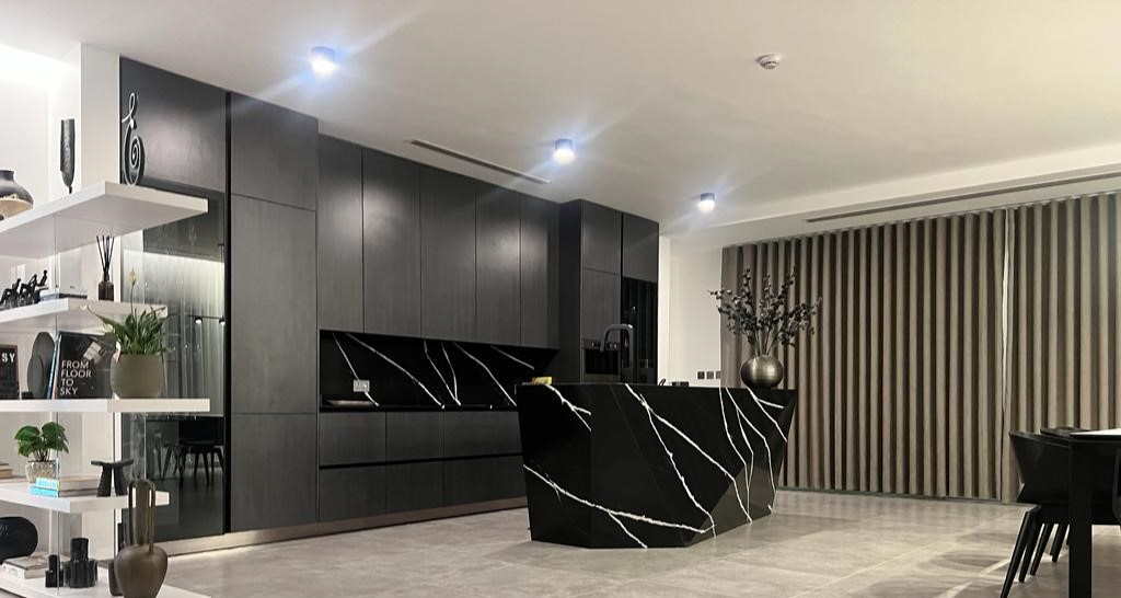 Modern kitchen interior with sleek black cabinetry, marble island, decorative shelving, and large window with curtains.