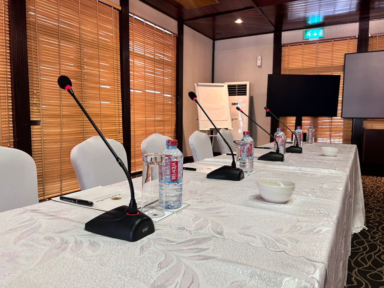 Woman in a modern office working on a laptop, with large monitors displaying colorful code, highlighting a tech-focused work environment.
