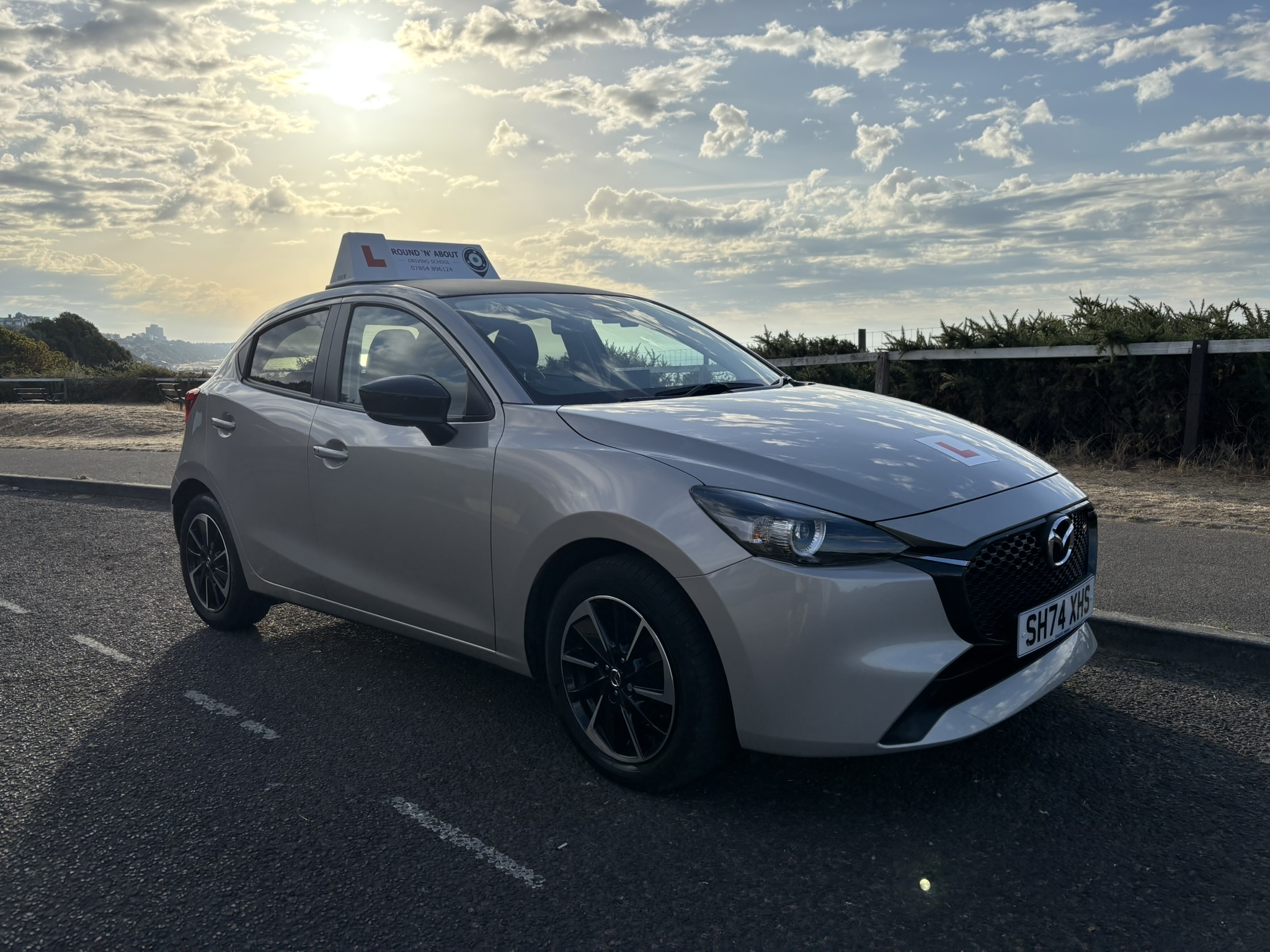 Silver Mazda driving school car parked by coastal road with ocean view and blue sky