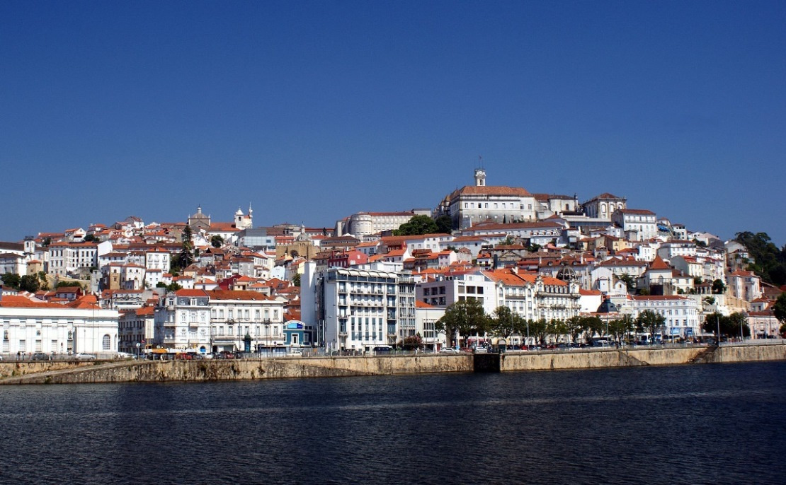 Obere Altstadt mit der Universität vom Fluss Mondego aus gesehen.
Coimbra, eine am Fluss gelegene Stadt in Zentralportugal und die ehemalige Hauptstadt des Landes, besitzt eine gut erhaltene mittelalterliche Altstadt und ist Heimat der historischen Universität Coimbra. Die auf dem Gelände eines ehemaligen Palastes erbaute Universität ist für ihre barocke Bibliothek, die Biblioteca Joanina, und den Glockenturm aus dem 18. Jahrhundert bekannt. In der Altstadt befindet sich die romanische Kathedrale Sé Velha, die im 12. Jahrhundert erbaut wurde.