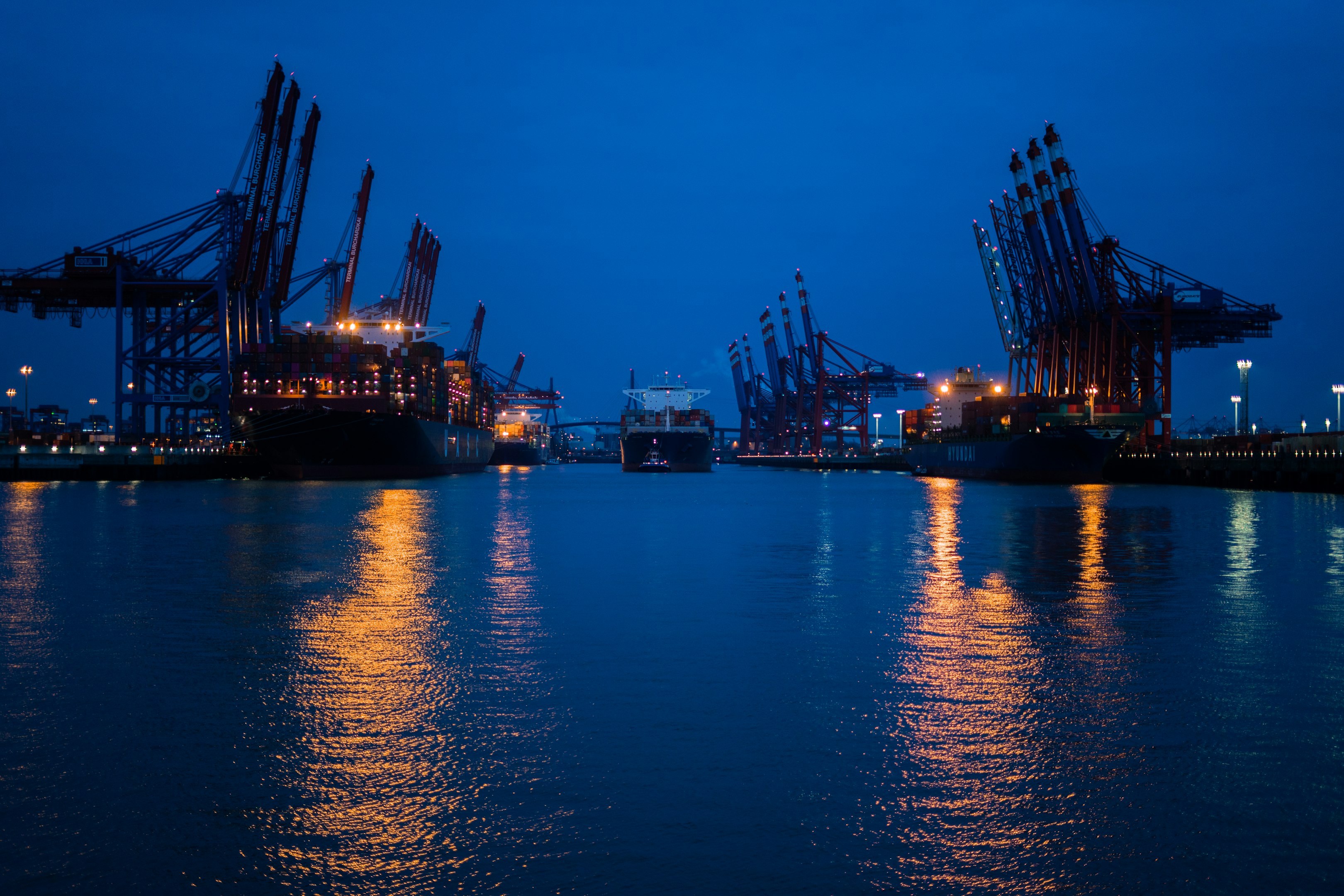 Large cargo ship transporting colorful shipping containers at sea during nighttime, city skyline visible on the horizon.