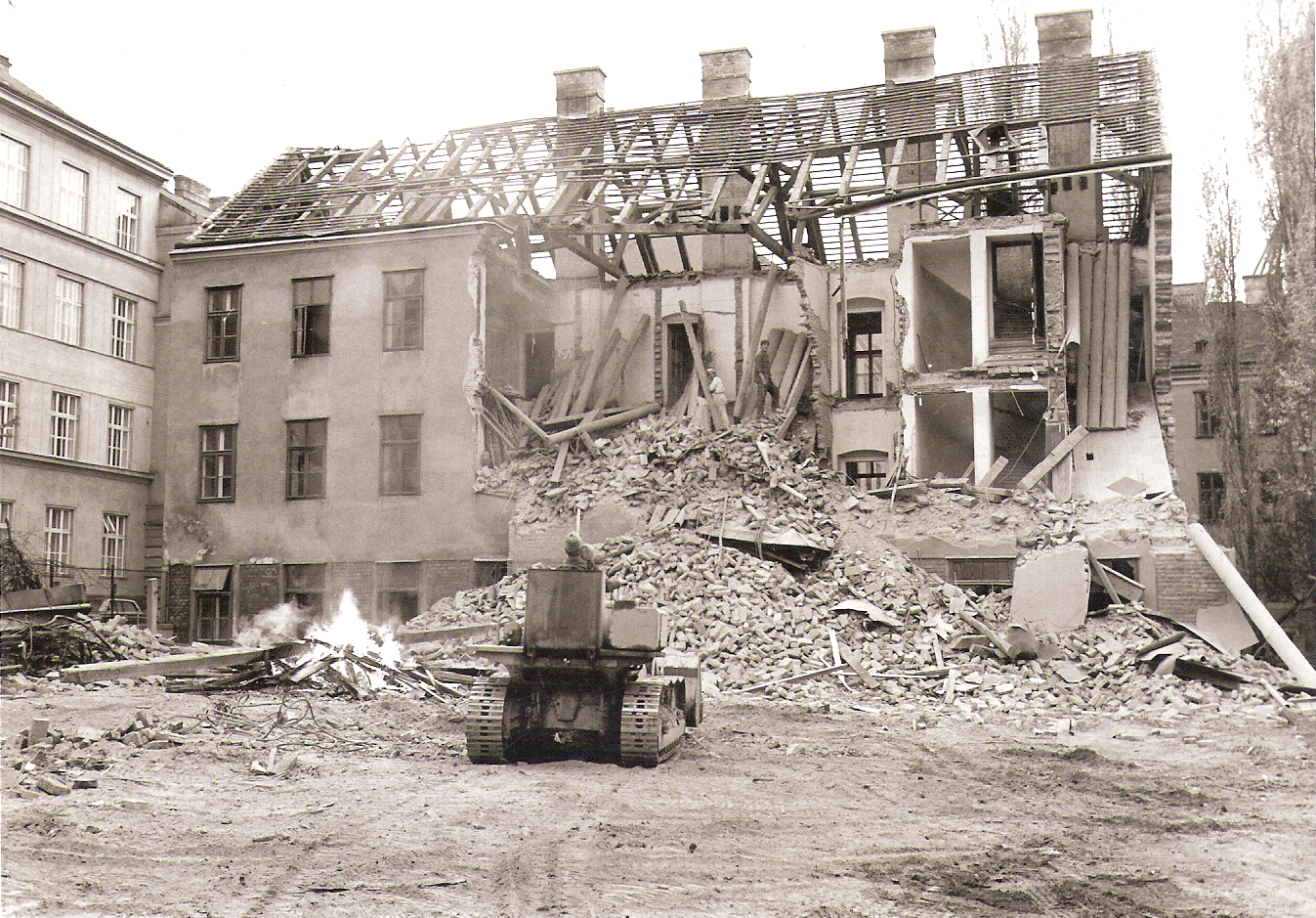 Baustelle mit gelbem Bagger, Kieshaufen und reflektierendem Wasser auf der Asphaltstraße in einer städtischen Umgebung.