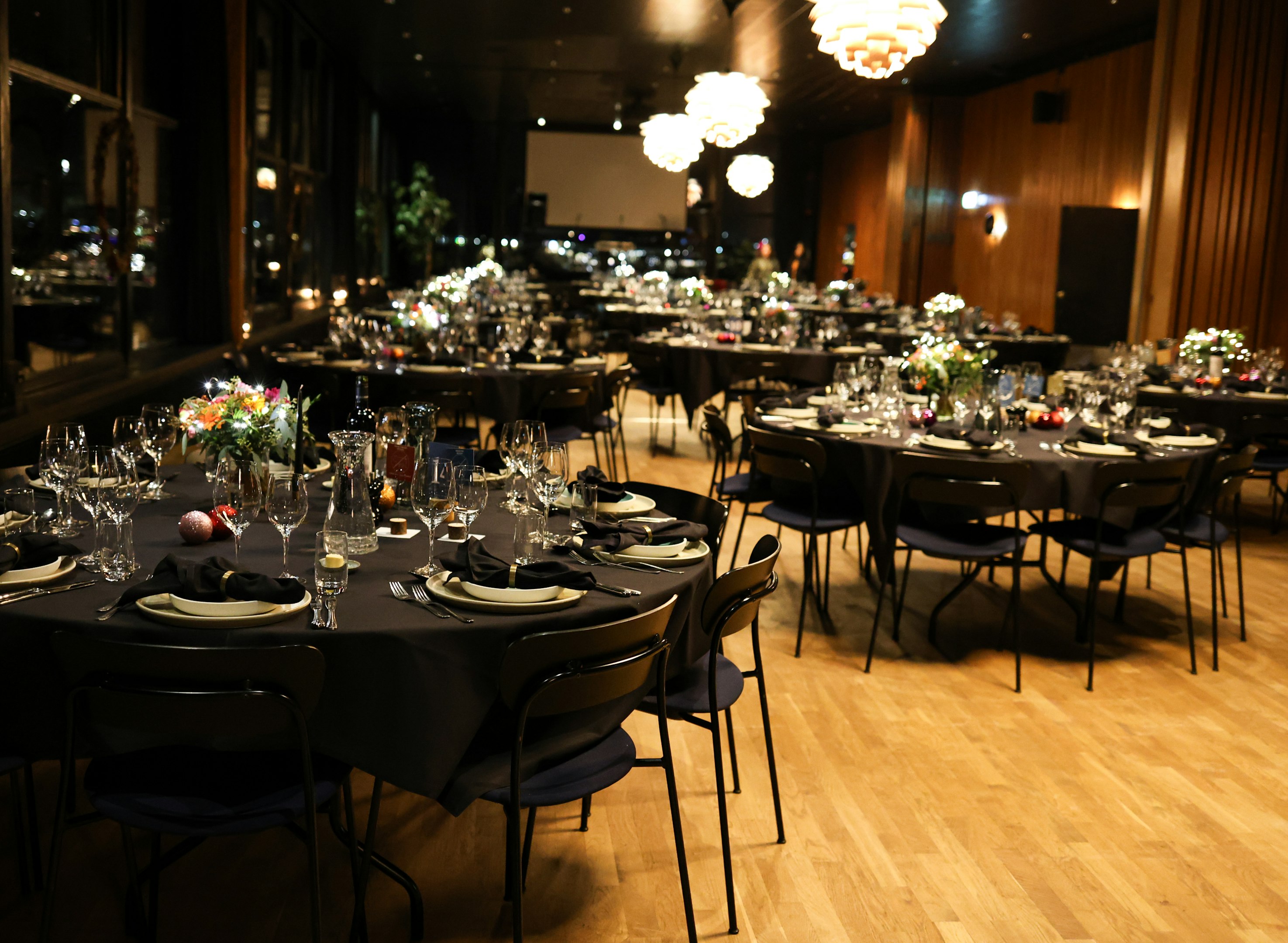 Modern restaurant interior with wooden furnishings, green plants hanging from ceiling, and neatly arranged dining tables set for guests.