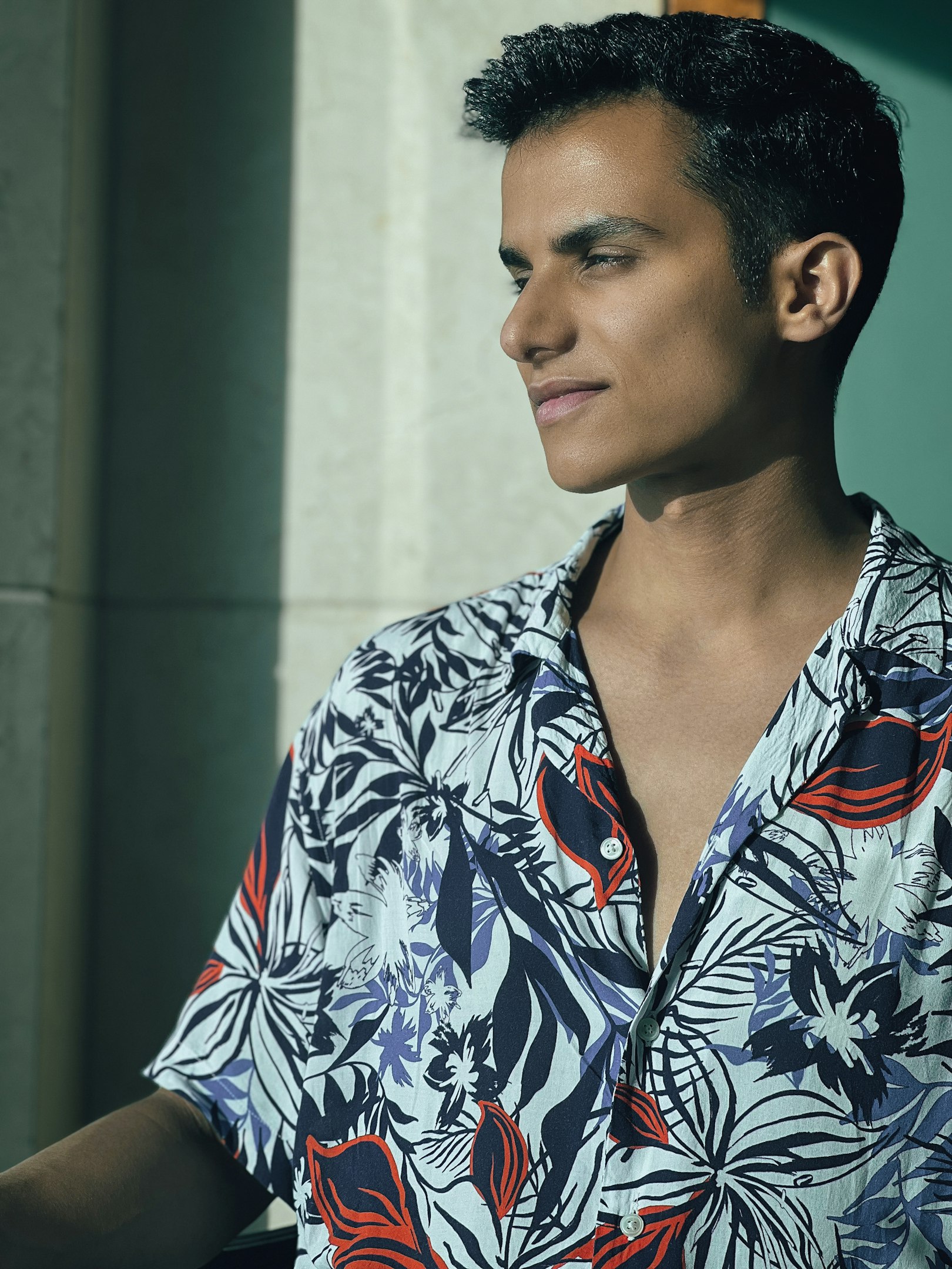 Young man in a floral shirt looking out a window in natural light