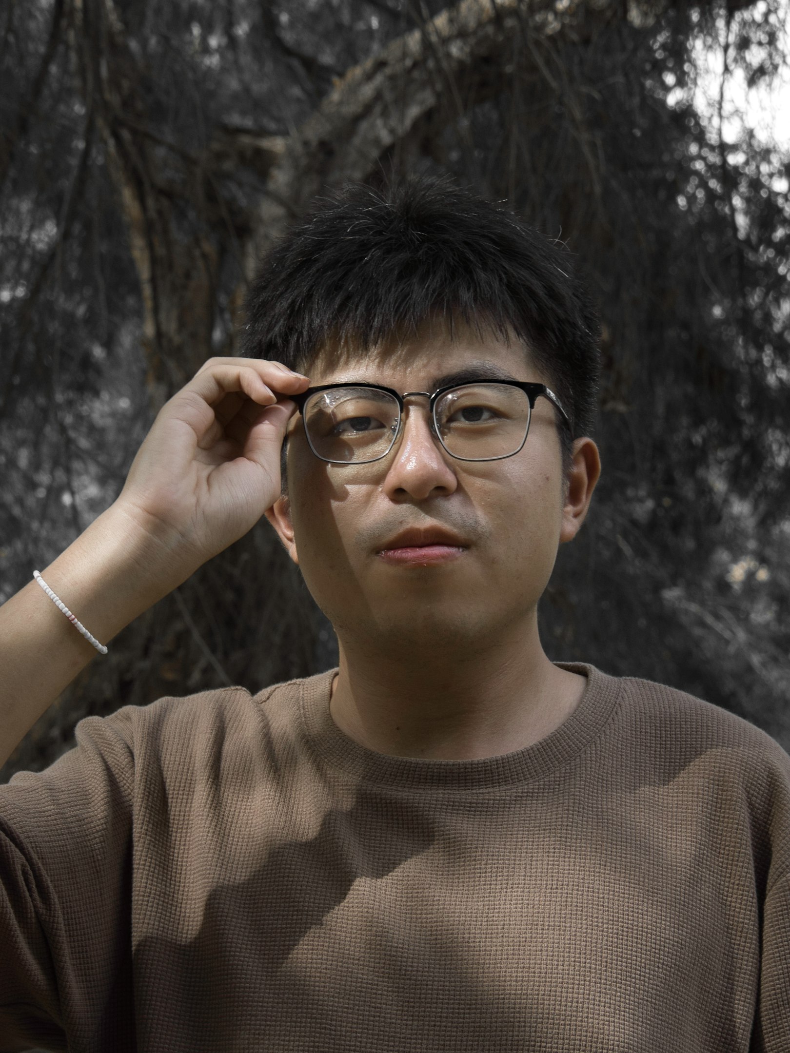 A man wearing glasses standing in front of a tree