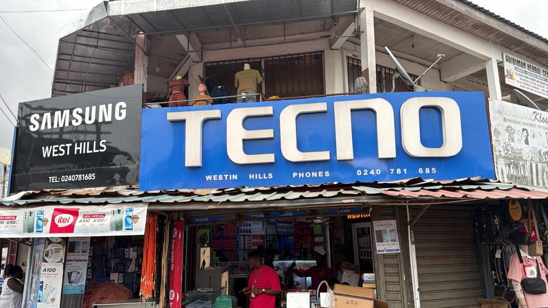 Modern glass building with palm trees lining an empty street at dusk, lit by streetlights.