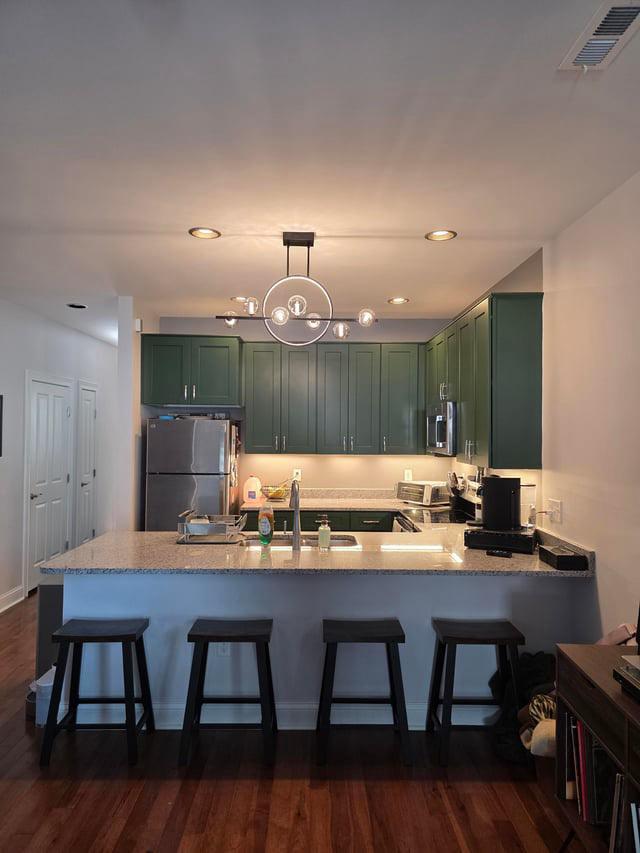 Modern open-concept kitchen and living room with wooden cabinets, island and bar stools, large windows, and cozy seating area.