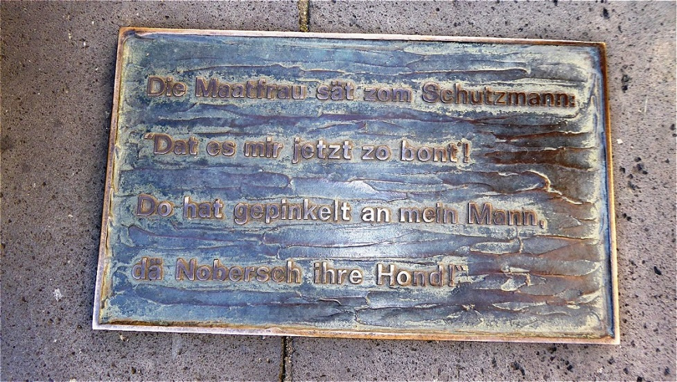 Die Maatfrau sät zom Schutzmann: „Dät es mir jetzt zo bont! Do hat gepinkelt an mein Mann, dä Nobersch ihre Hond!“
Die Marktfrau sagt zum Schutzmann. „Das ist mir jetzt zu bunt, da hat der Hund der Nachbarin auf meinen Mann gepinkelt!
