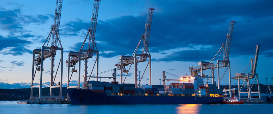 Large cargo ship docked at a port with cranes and shipping containers at dusk.