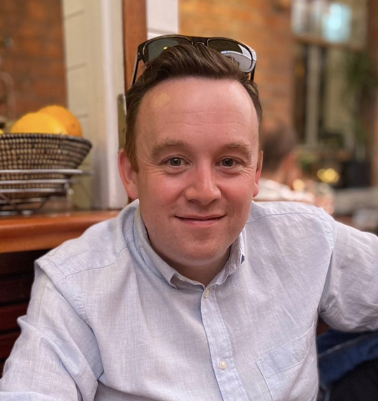 RTÉ journalist Fran McNulty smiles to camera. He has a pair of sunglasses on his head.