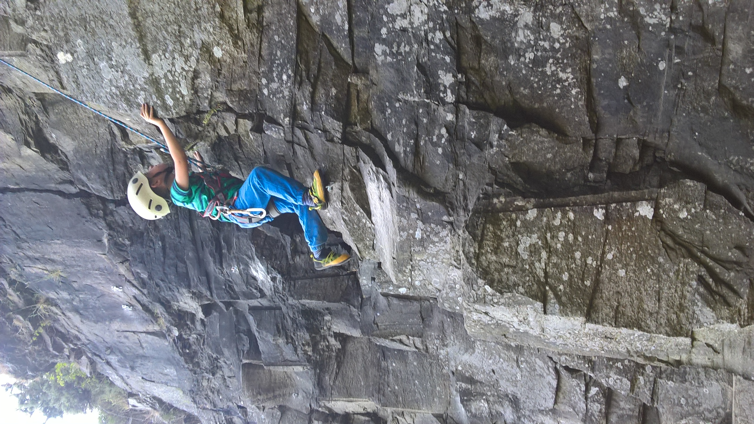 Person standing near orange tent inside cave with waterfall and mountain view.